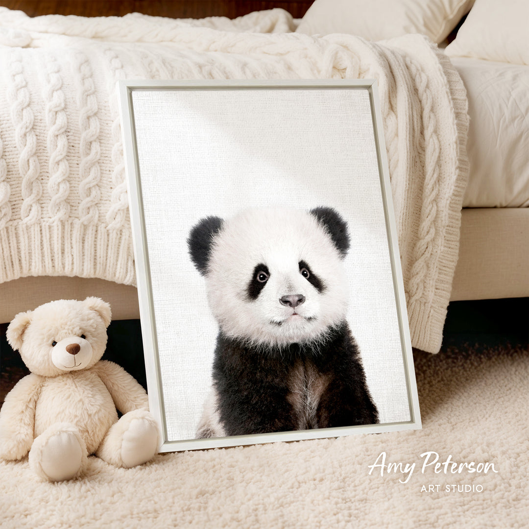A framed photograph of a panda bear is displayed on a bed, accompanied by a teddy bear.