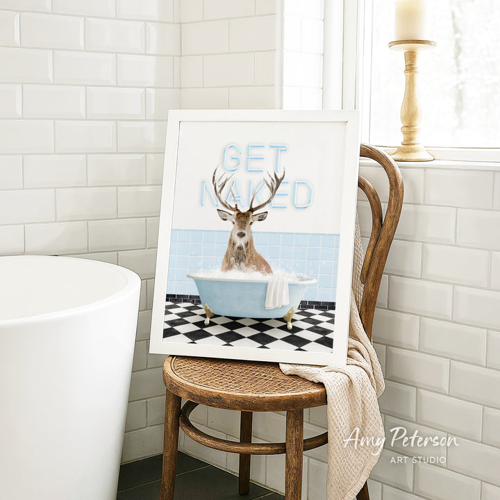 A framed image of a deer sitting in a bathtub with the text "GET NAUGED" on it, placed on a wooden chair in a bathroom setting.