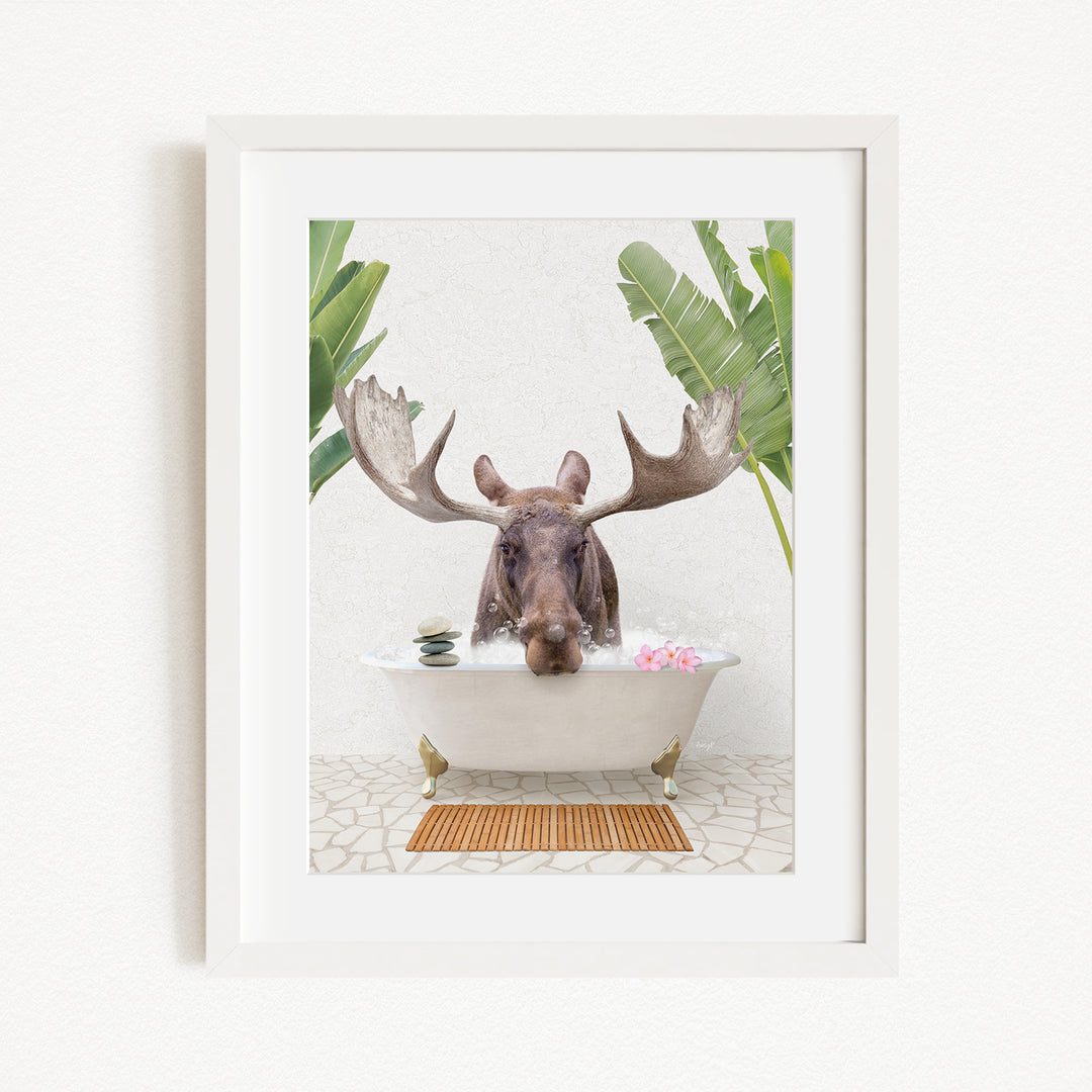 A moose with large antlers is sitting in a bathtub filled with water and bubbles, surrounded by tropical plants.