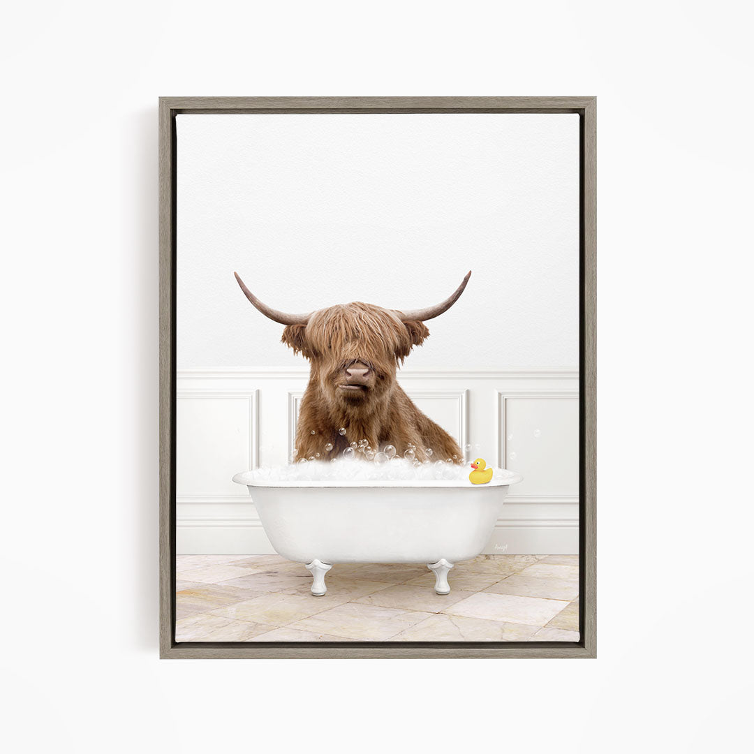 A brown cow with long horns is sitting in a white bathtub filled with water, with a yellow rubber duck floating in the tub.