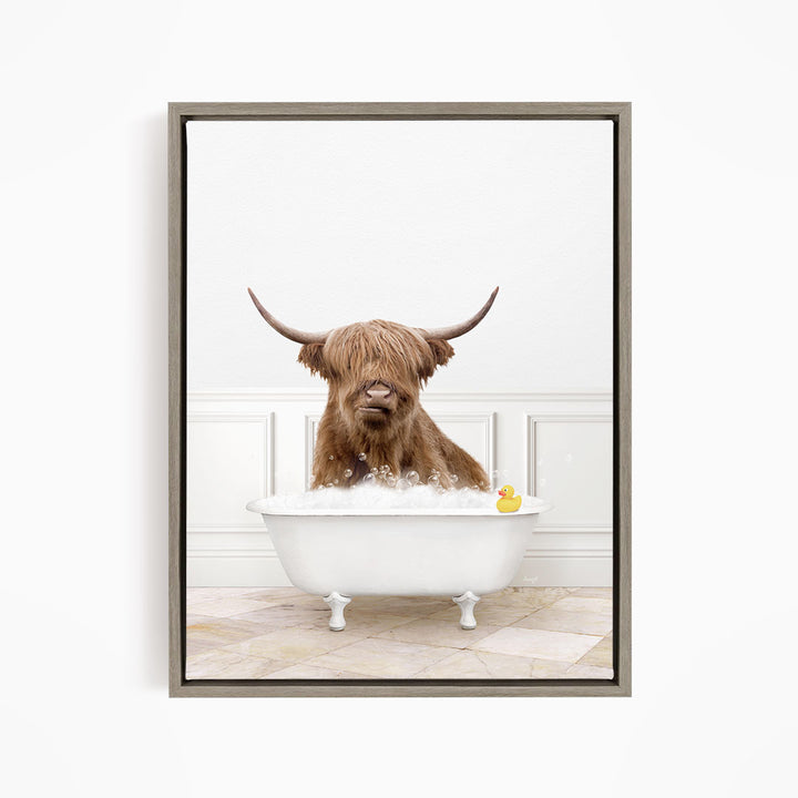 A brown cow with long horns is sitting in a white bathtub filled with water, with a yellow rubber duck floating in the tub.