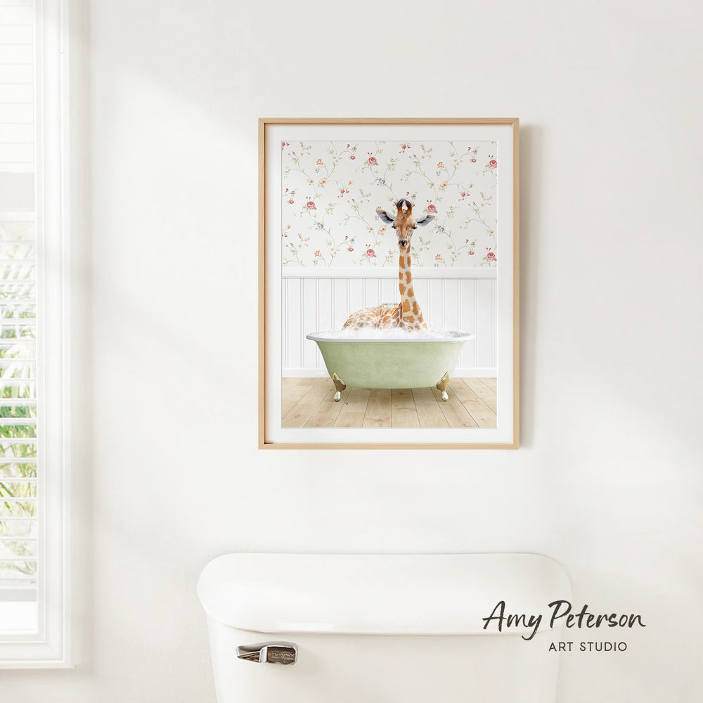A framed image of a giraffe sitting in a green bathtub, with a floral pattern on the wall behind it.