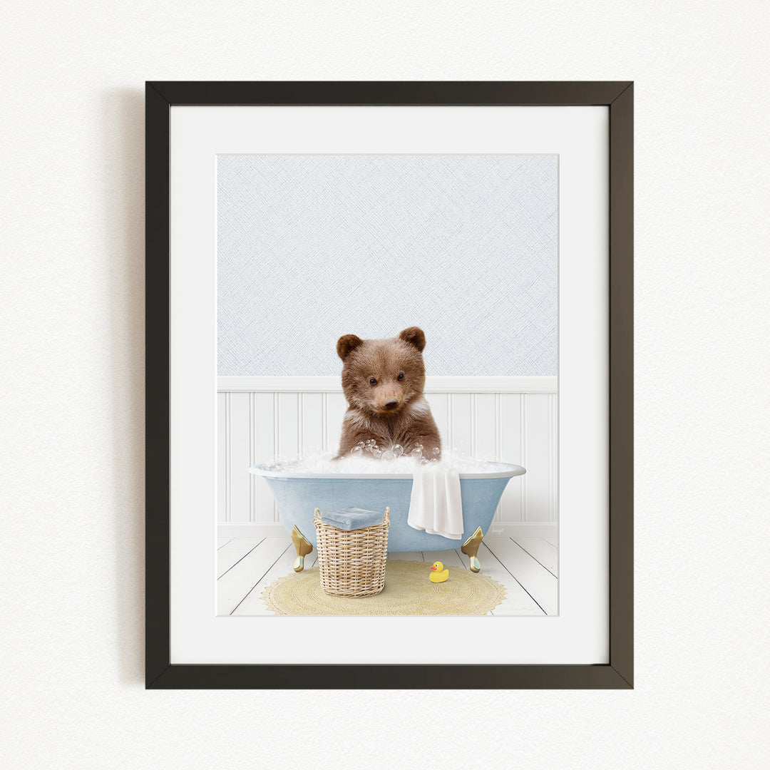 A cute brown bear sitting in a blue bathtub, surrounded by a yellow rubber duck and a basket of bath toys.