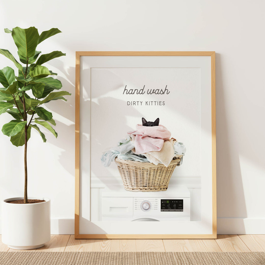 A framed poster with a cat sitting in a basket of laundry, accompanied by the text "hand wash dirty kittens".