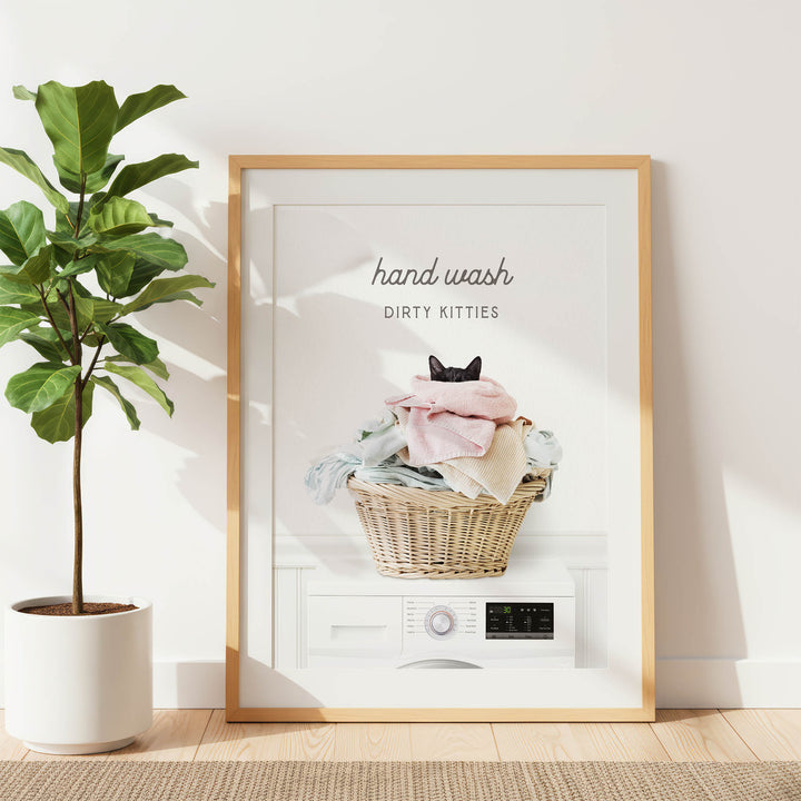 A framed poster with a cat sitting in a basket of laundry, accompanied by the text "hand wash dirty kittens".