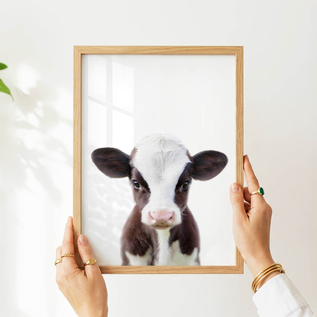 A person's hands are holding a wooden frame with a picture of a cow inside it.