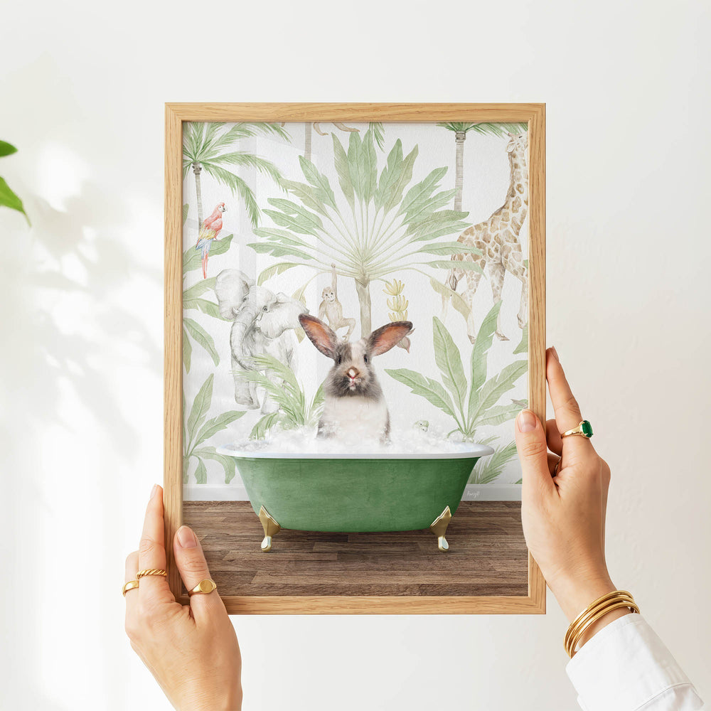 A person's hands are holding a framed picture of a rabbit sitting in a green bathtub, surrounded by tropical plants and animals.