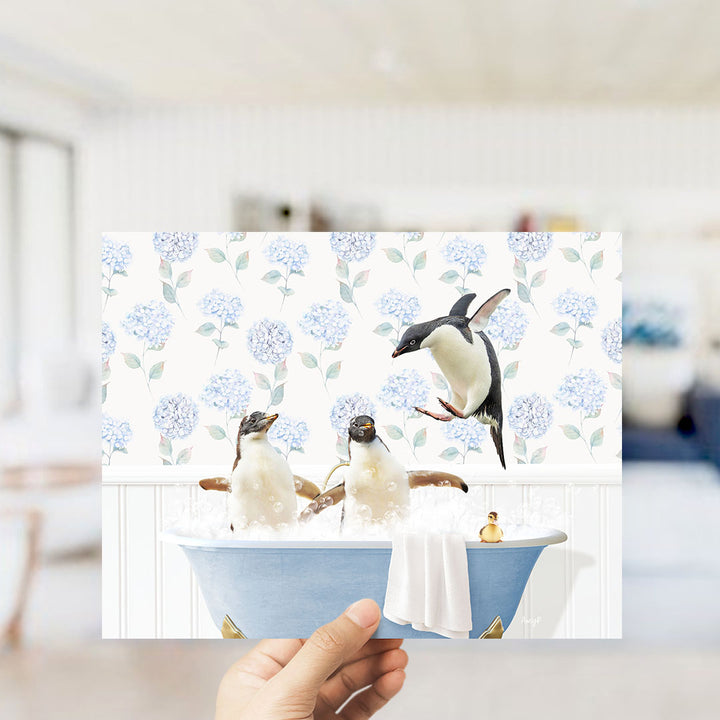 A hand holds up a collage of three images depicting penguins in a bathtub, with one penguin flying above the others.