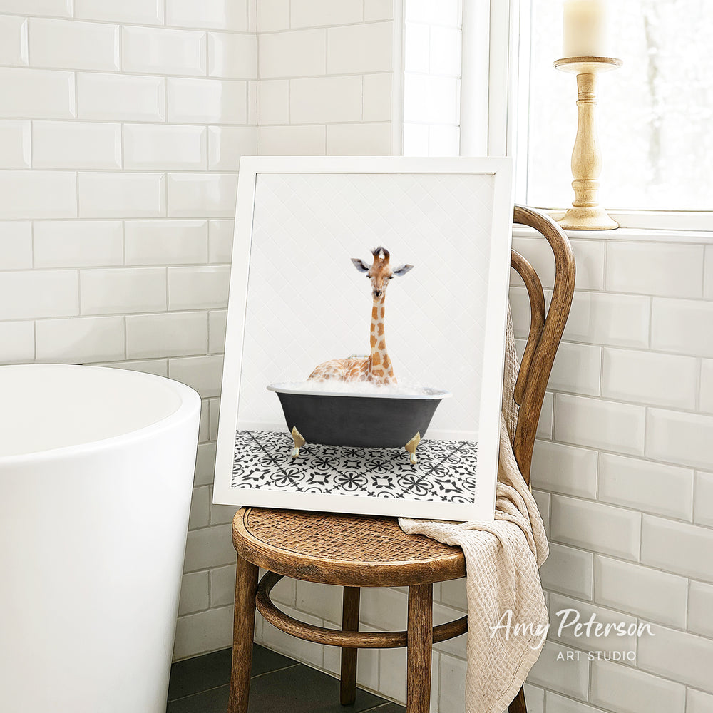 A framed image of a giraffe sitting in a bathtub, surrounded by a patterned tile floor, is displayed on a wooden chair in a bathroom setting.