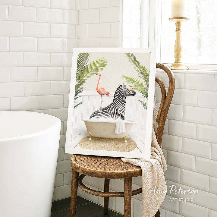 A framed painting of a zebra sitting in a bathtub, surrounded by tropical plants, is displayed on a wooden chair in a bathroom setting.