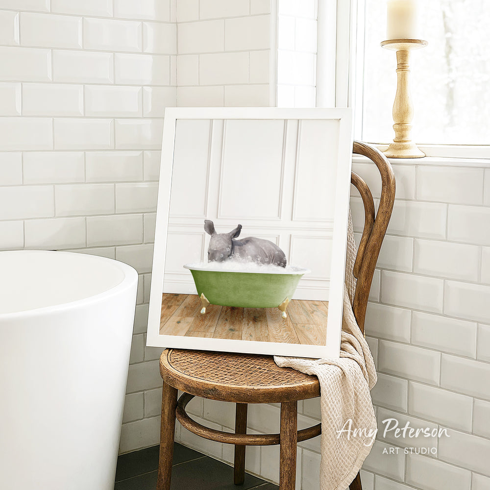 A framed image of a gray rabbit sitting in a green bathtub, with a wooden chair and a white tiled wall in the background.