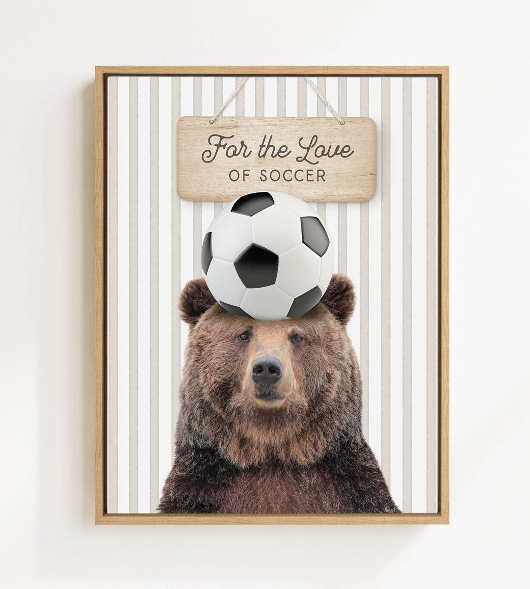 A framed image of a brown bear with a soccer ball on its head, accompanied by a wooden sign that reads "For the Love of Soccer".