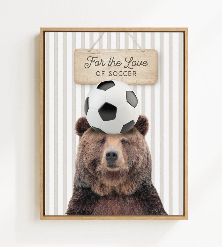 A framed image of a brown bear with a soccer ball on its head, accompanied by a wooden sign that reads "For the Love of Soccer".