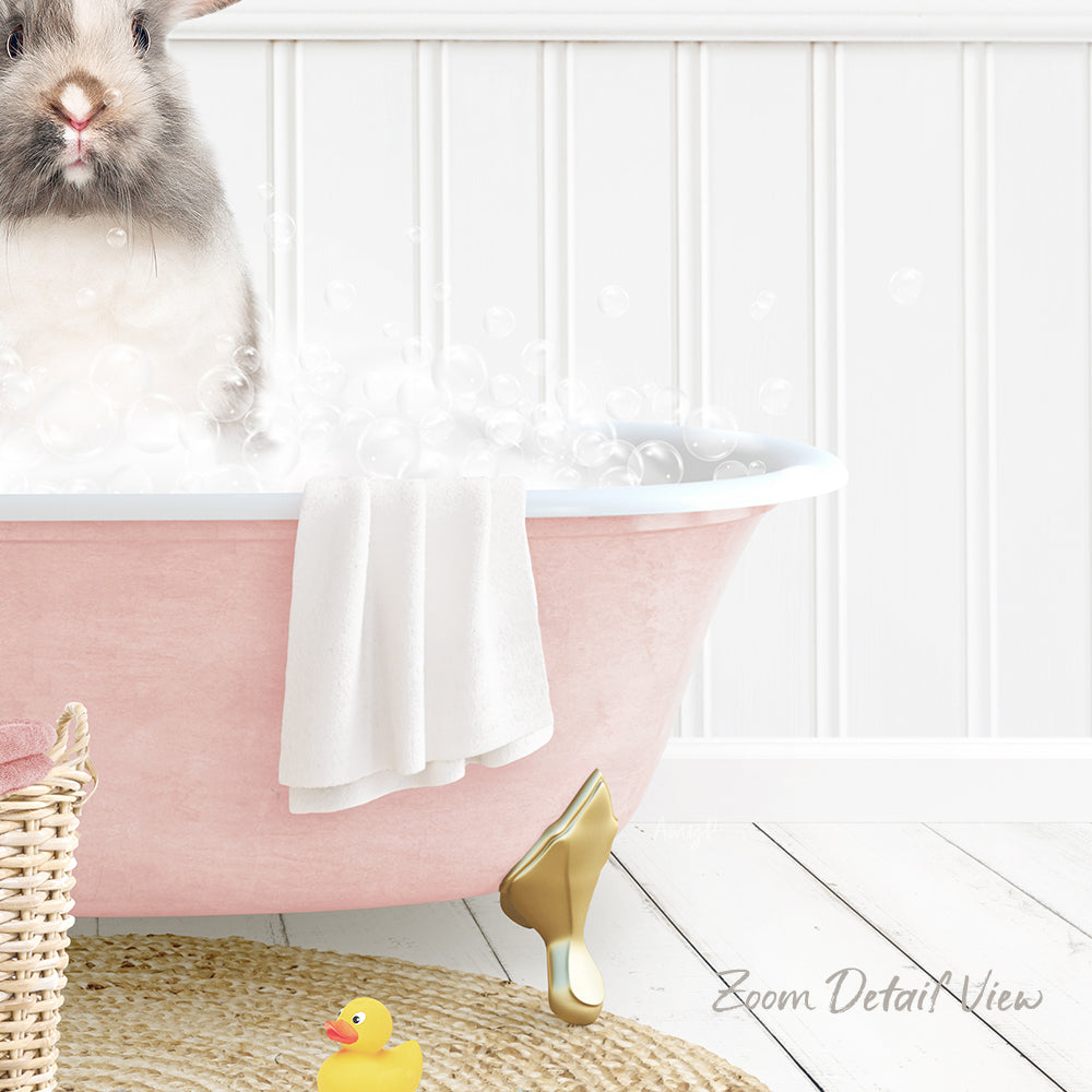 A fluffy gray rabbit sitting in a pink bathtub filled with bubbles, surrounded by a yellow rubber duck and a white towel.