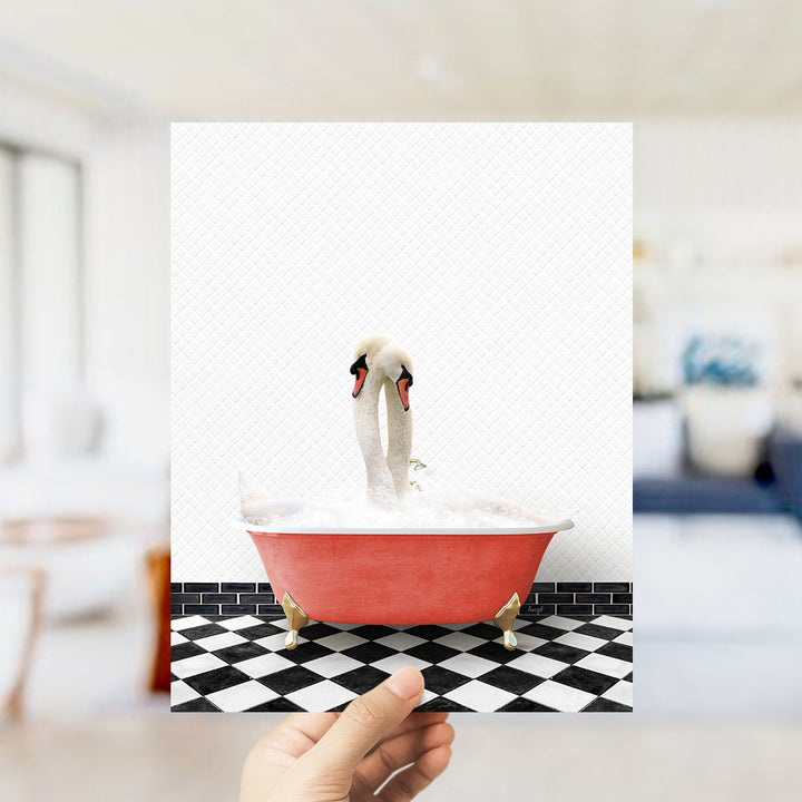 A hand holds up a framed image of two swans sitting in a red bathtub on a black and white checkered floor.