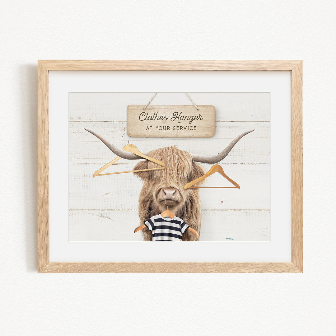 A framed image depicting a large, furry animal with long horns, wearing a striped shirt and surrounded by hanging clothes hangers.