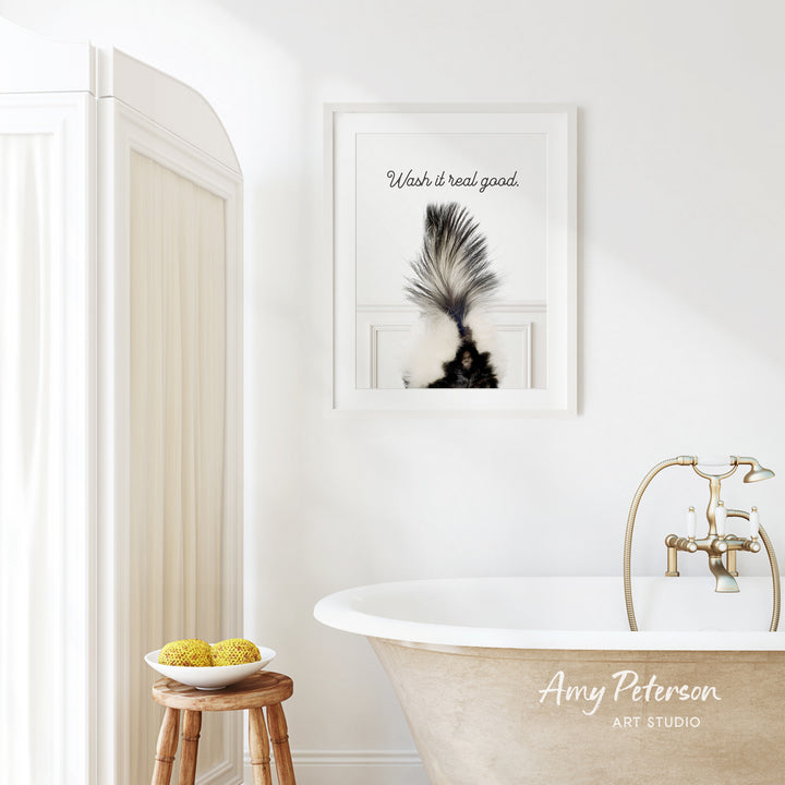a bathroom with a framed picture of a skunk on the wall, a wooden stool with a bowl of fruit, and a clawfoot bathtub.