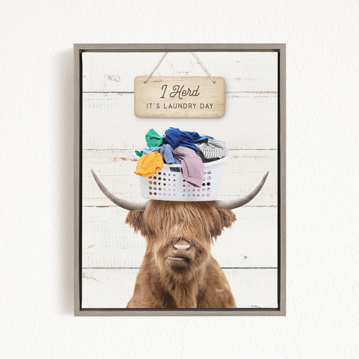 A humorous image of a Highland cow with a basket of laundry on its head, accompanied by a wooden sign that reads "I herd it's laundry day".