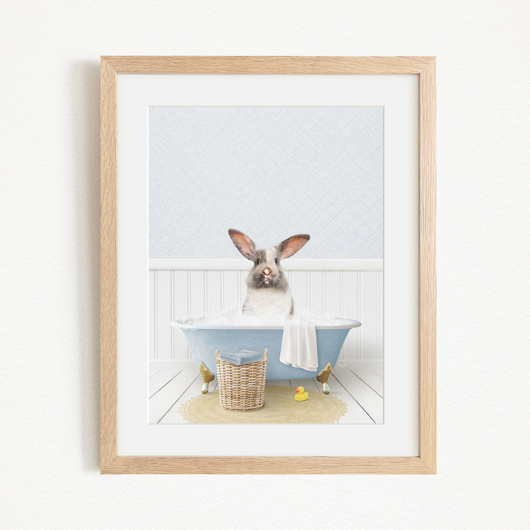 A white rabbit sitting in a blue bathtub filled with bubbles, surrounded by a yellow rubber duck and a basket.