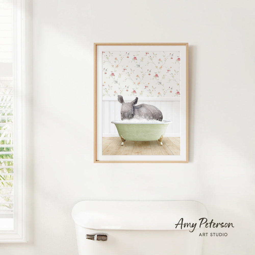 A framed print of a gray rhinoceros sitting in a green bathtub, with a floral pattern on the wall behind it.
