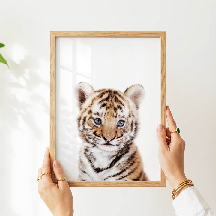 A person's hands are holding a wooden frame with a picture of a young tiger inside it.