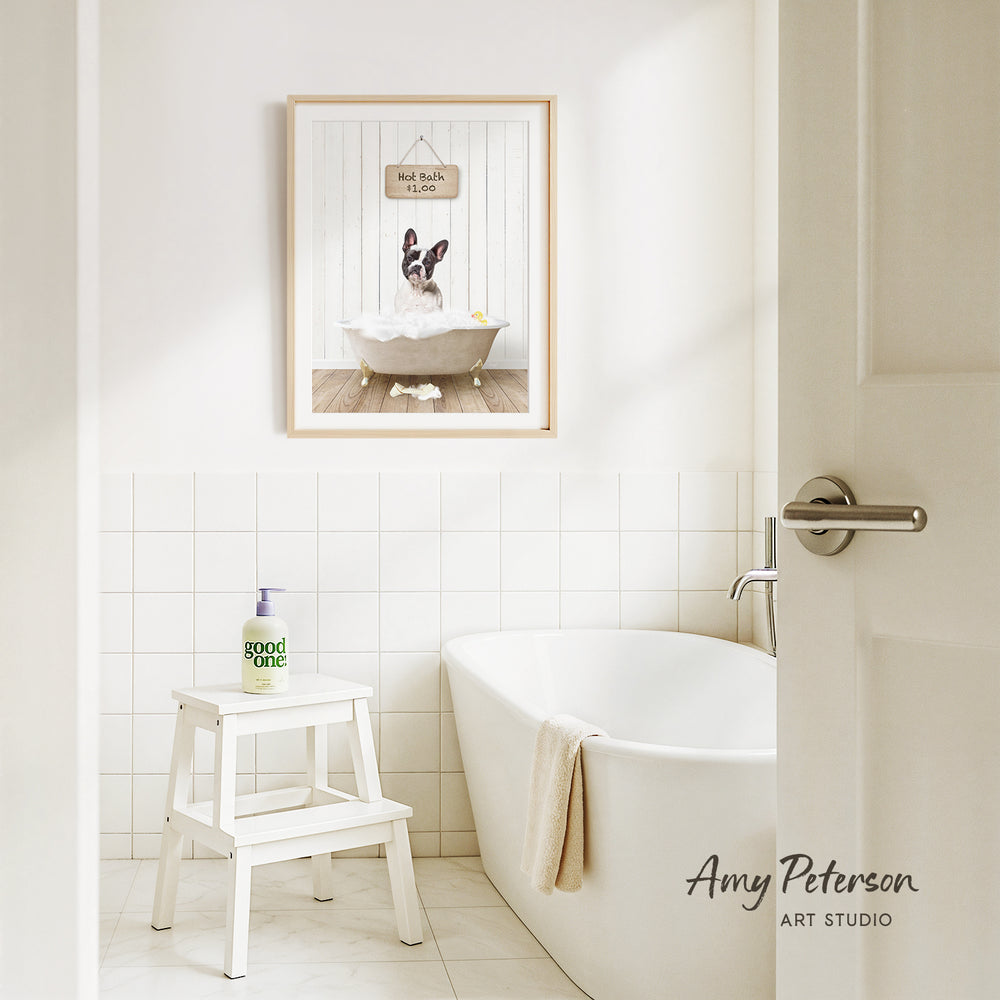 A framed picture of a dog sitting in a bathtub, with a sign above it that says "Hot bath $1.00". The bathroom has a white bathtub, a stool, and a towel hanging on the side of the tub.