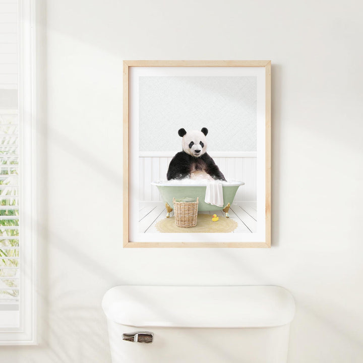 A panda bear sitting in a bathtub, surrounded by a basket of toys and a towel, is the central focus of the framed image displayed on the wall.