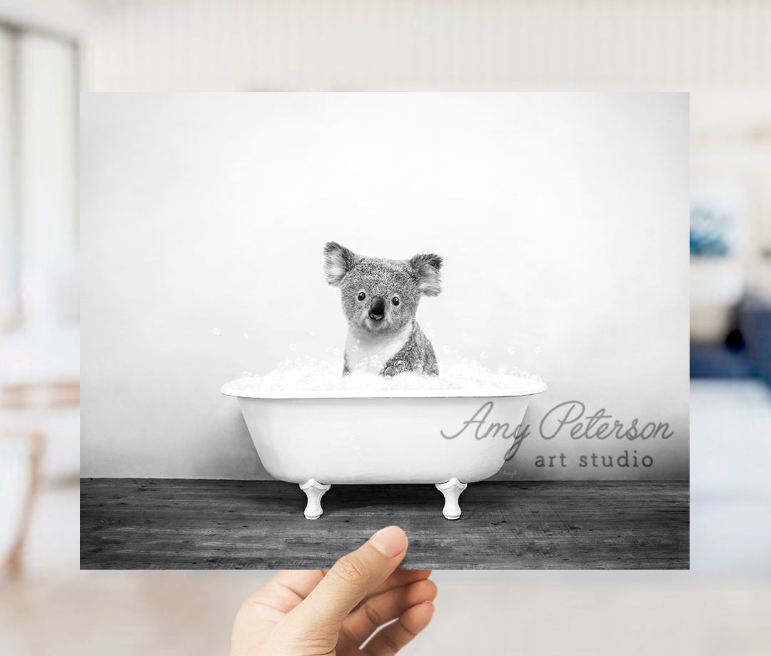 a hand holding up a photo of a koala in a bathtub