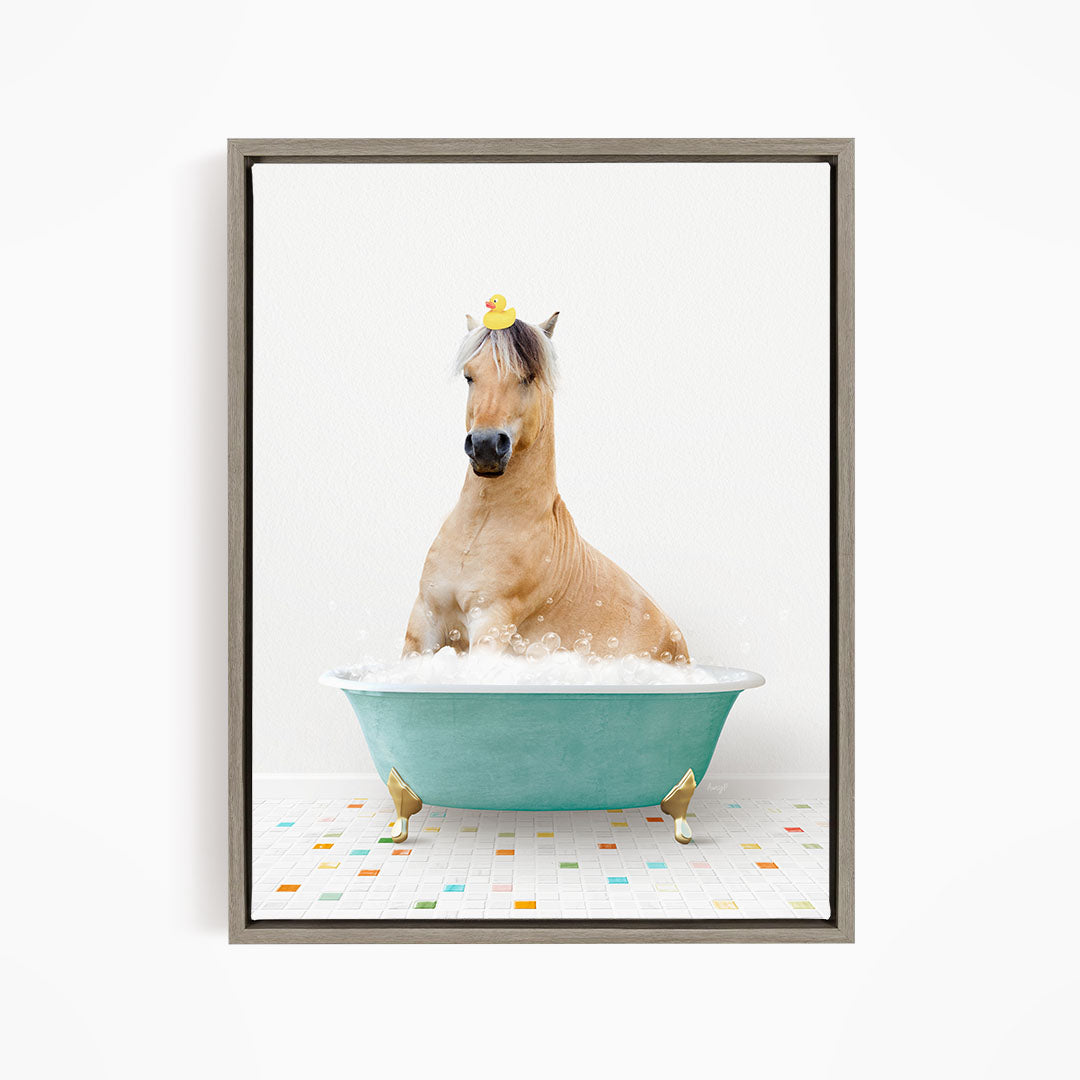 A light brown horse is sitting in a blue bathtub filled with bubbles, wearing a yellow rubber duck on its head.
