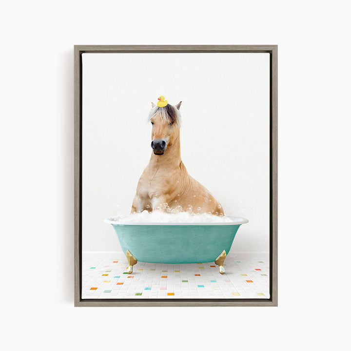 A light brown horse is sitting in a blue bathtub filled with bubbles, wearing a yellow rubber duck on its head.