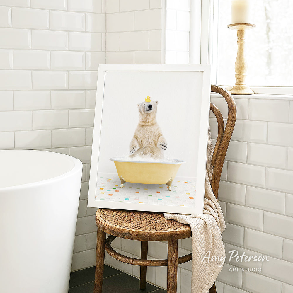 A framed image of a polar bear sitting in a bathtub, with a yellow rubber duck floating on its head, is displayed on a wooden chair in a bathroom setting.