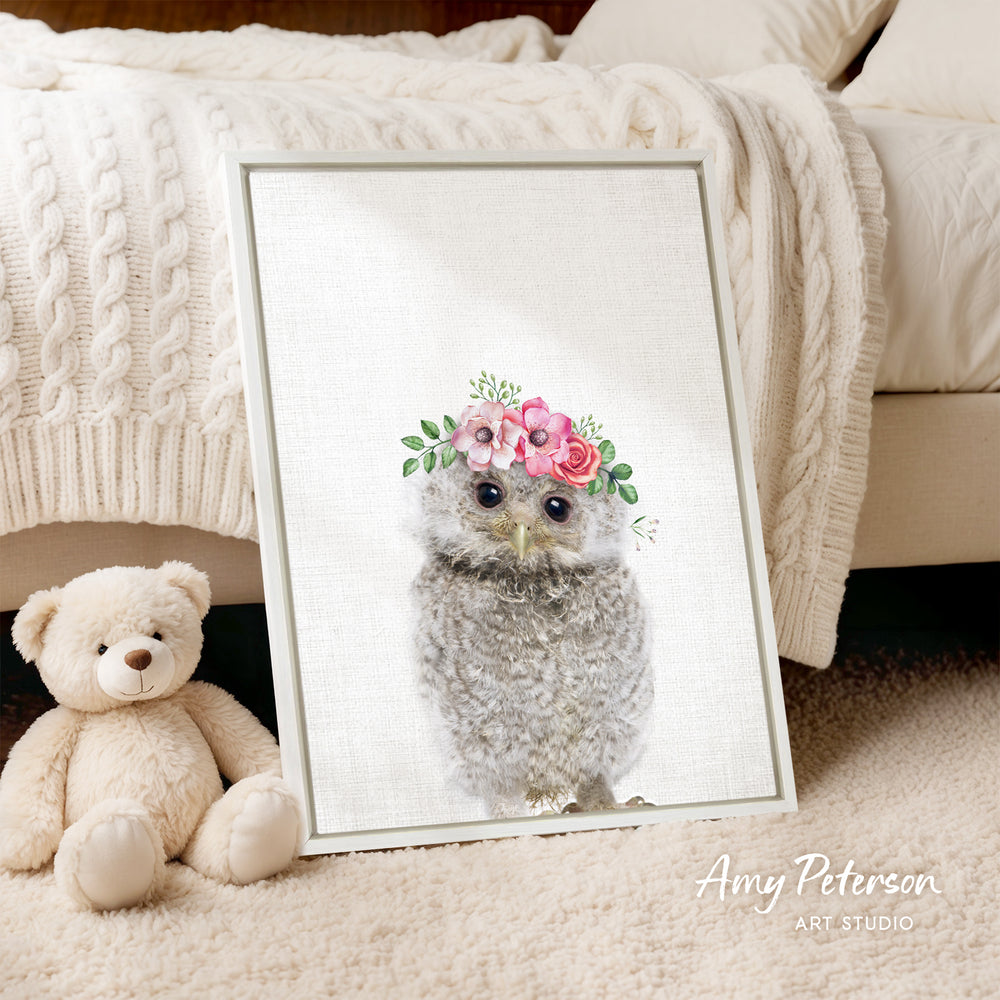 A framed print of an owl wearing a flower crown is displayed on a beige carpet, accompanied by a teddy bear.