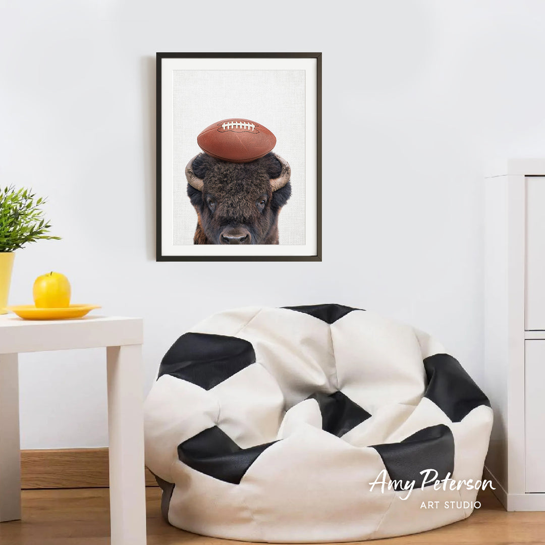 a framed picture of a buffalo with a football on its head, hanging on a white wall above a black and white bean bag chair.