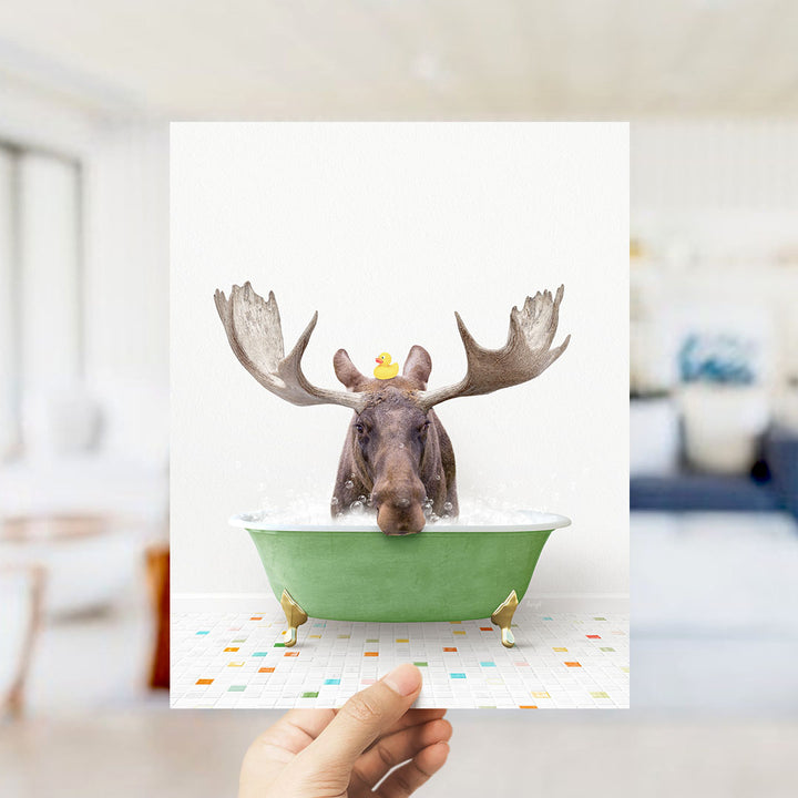 A moose with large antlers is sitting in a green bathtub filled with bubbles, with a yellow rubber duck floating on its head.