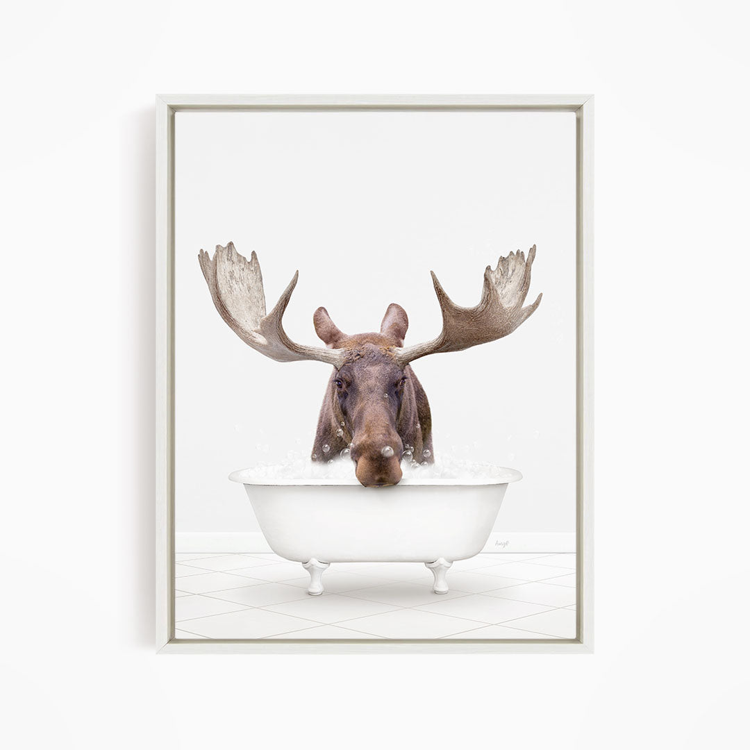 A moose with large antlers is sitting in a white bathtub filled with water, creating a whimsical and humorous scene.