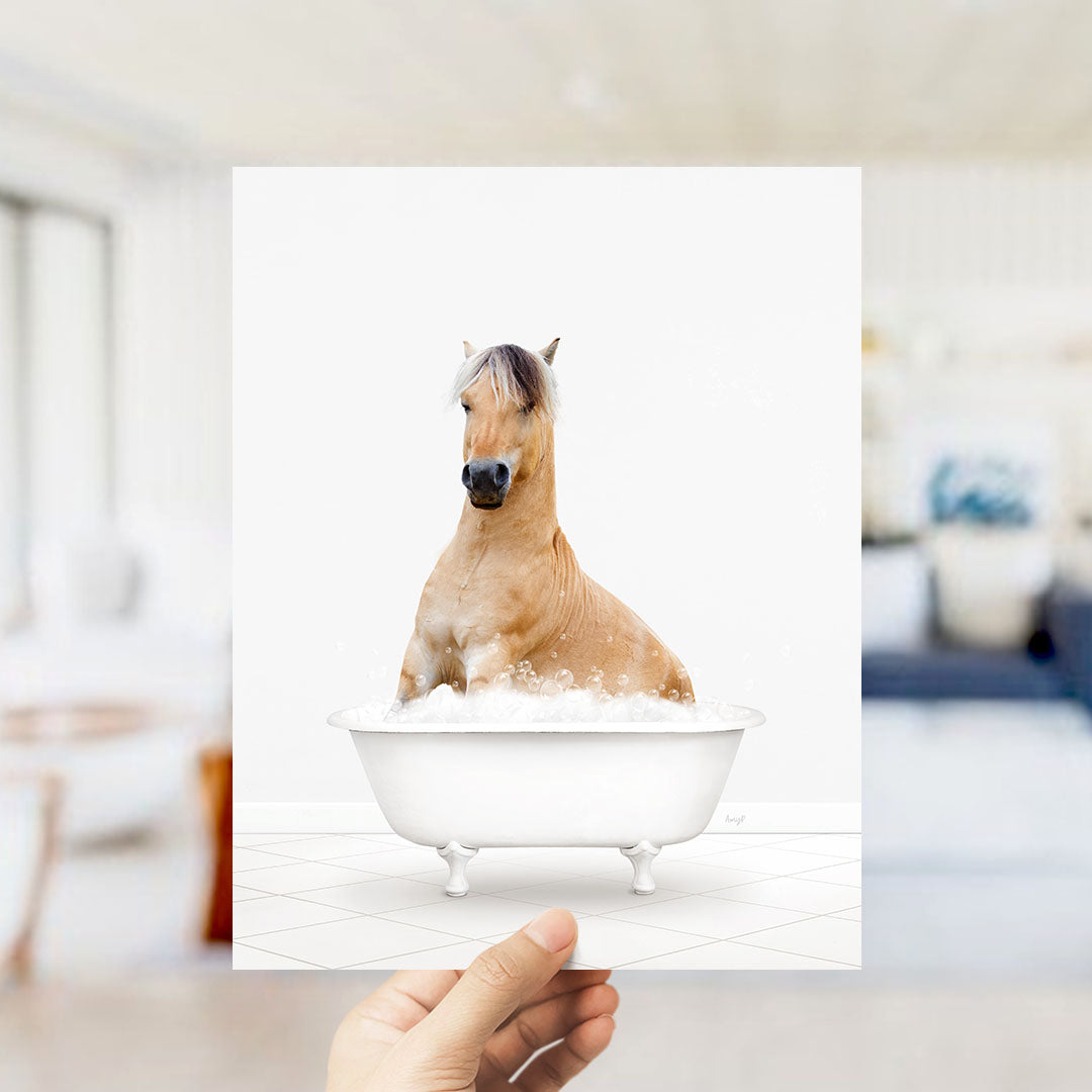 A hand holds up a framed image of a horse sitting in a bathtub filled with water.