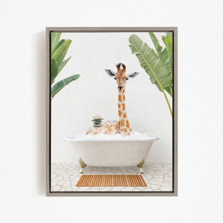 A giraffe is sitting in a white bathtub filled with bubbles, surrounded by green leaves and a wooden mat on the floor.