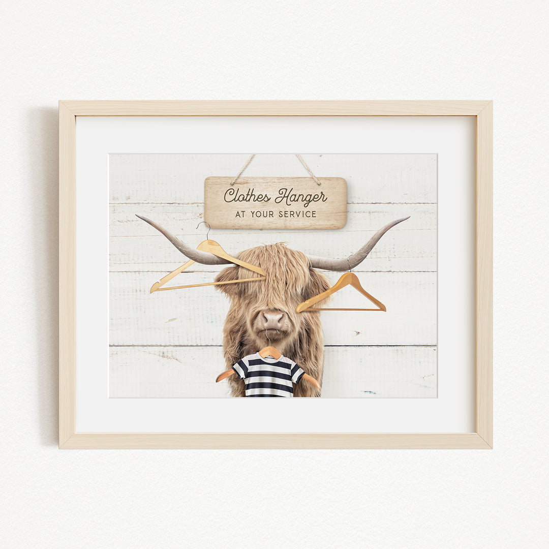 A framed image depicting a large, furry animal with a sign that reads "Clothes Hanger at your service" in front of it.