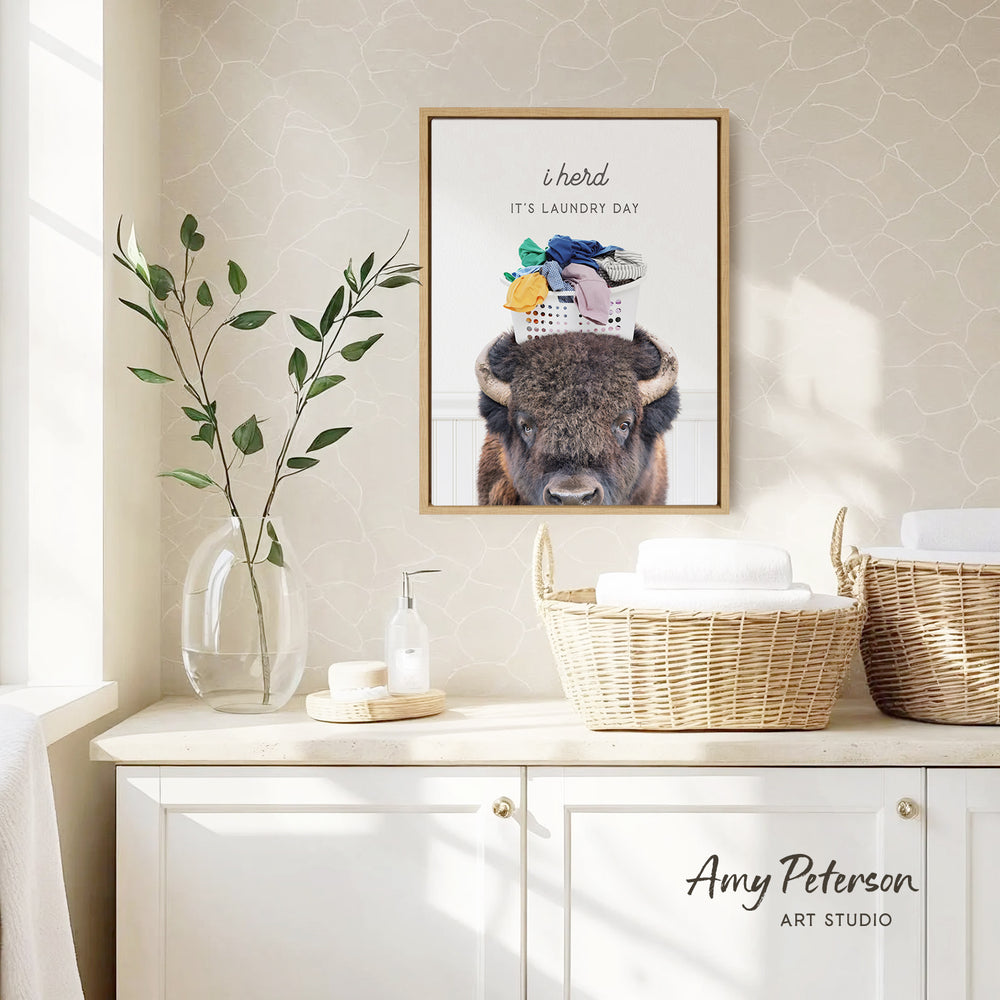a framed poster of a bison with a laundry basket on its head, hanging on a wall above a white cabinet.