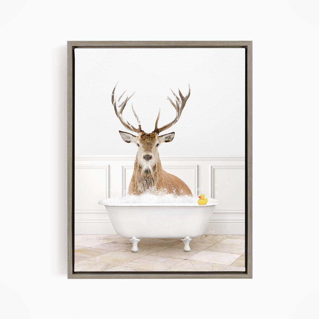 A deer with large antlers is sitting in a white bathtub filled with water, with a rubber duck floating in the tub.