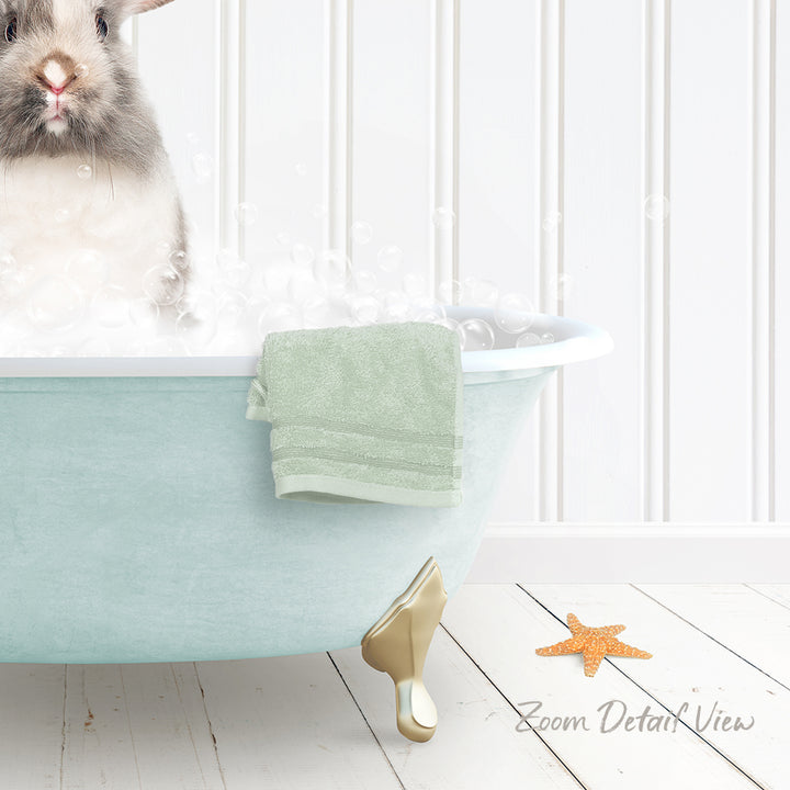 A small rabbit sitting in a light blue bathtub filled with bubbles, with a towel and starfish nearby.