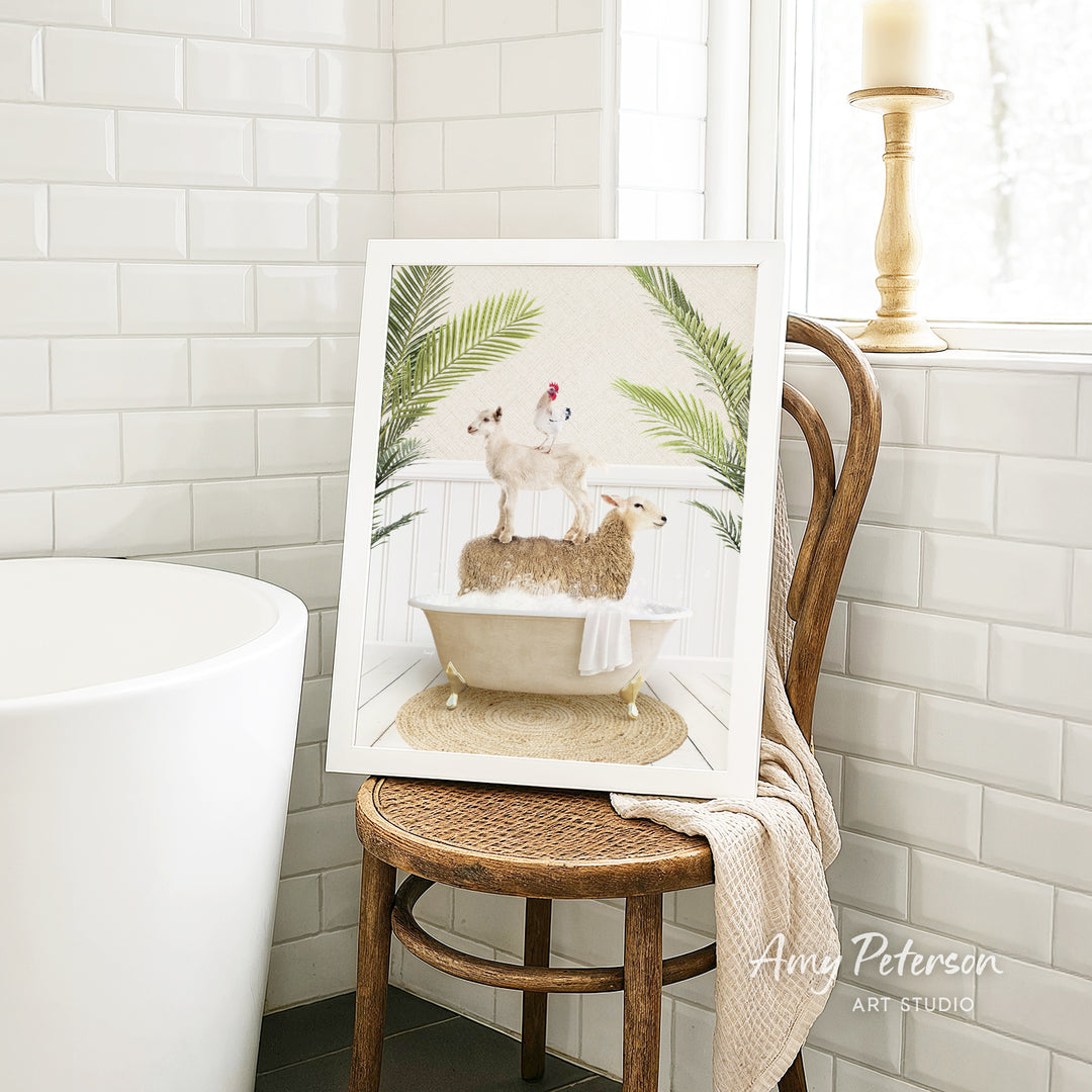 A framed image of a sheep standing on a bathtub, surrounded by palm leaves, is displayed on a wooden chair in a bathroom setting.