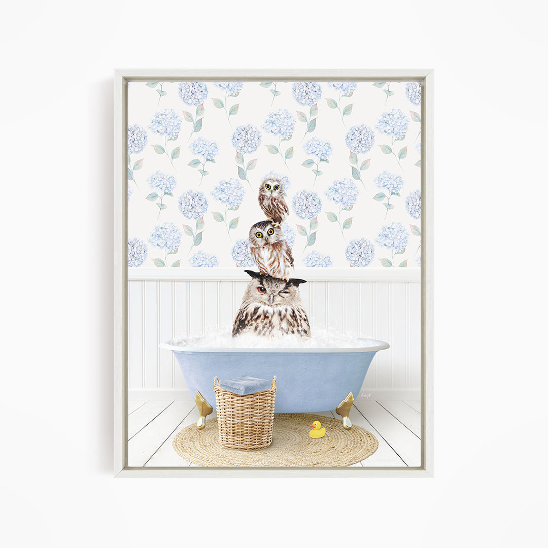 A framed image depicting three owls sitting in a bathtub filled with bubbles, surrounded by a blue floral pattern on the wall.