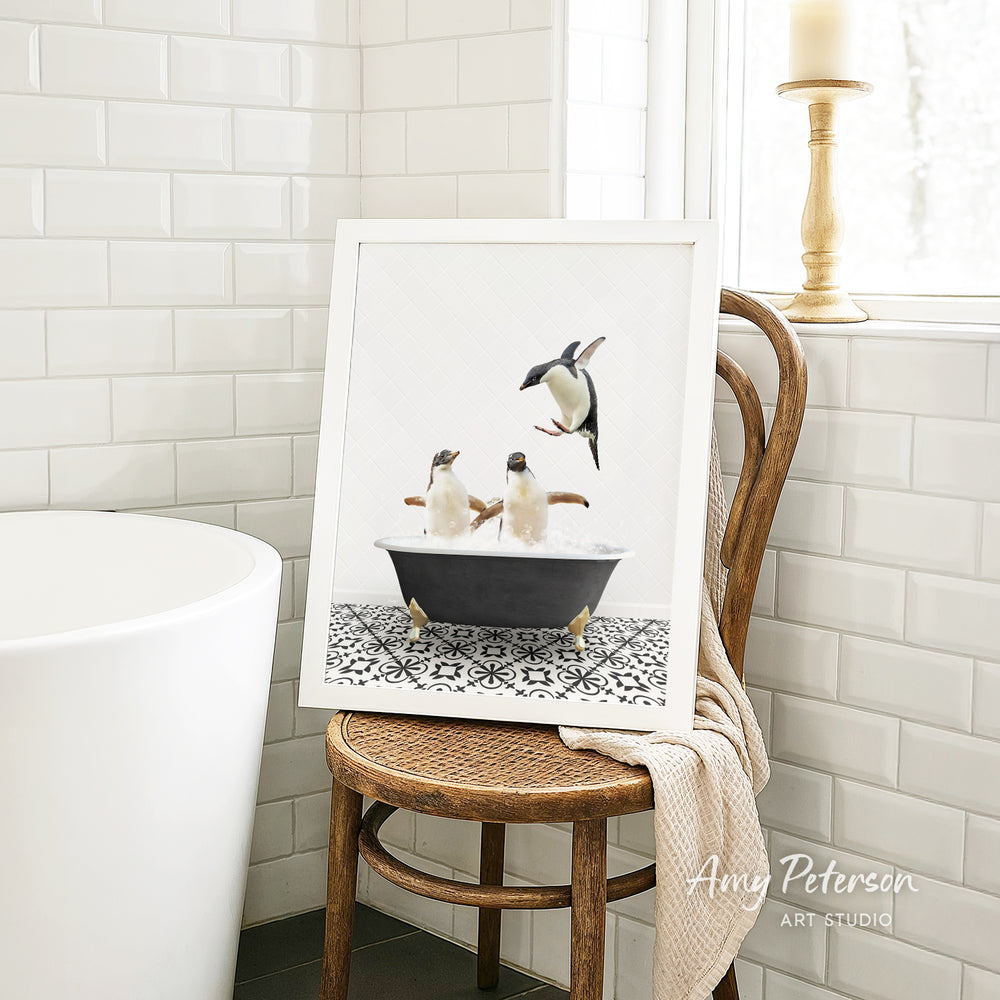 A framed image of two penguins sitting in a bathtub, surrounded by a black and white patterned tile floor, is displayed on a wooden chair in a bathroom setting.
