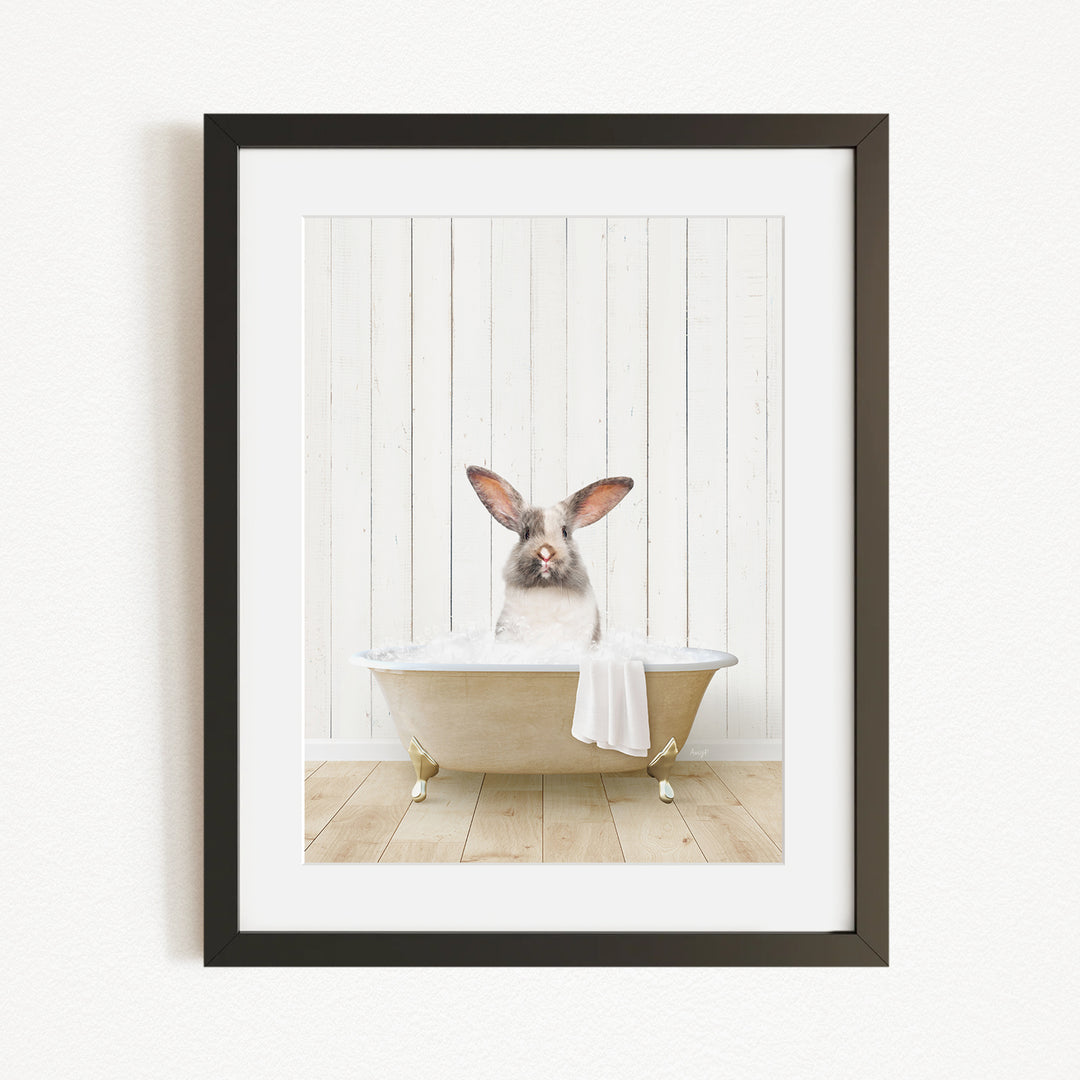 A white rabbit sitting in a bathtub, with its head in the water, against a white wooden background.
