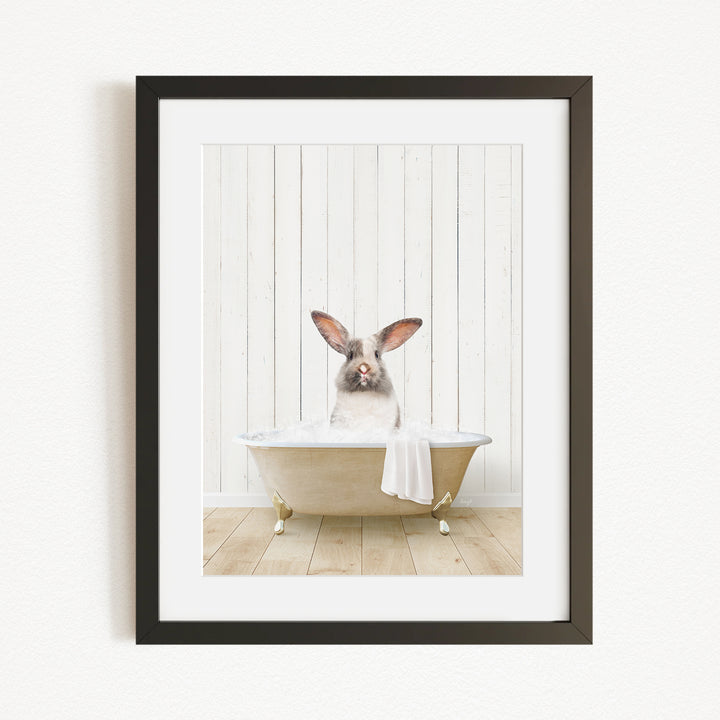 A white rabbit sitting in a bathtub, with its head in the water, against a white wooden background.