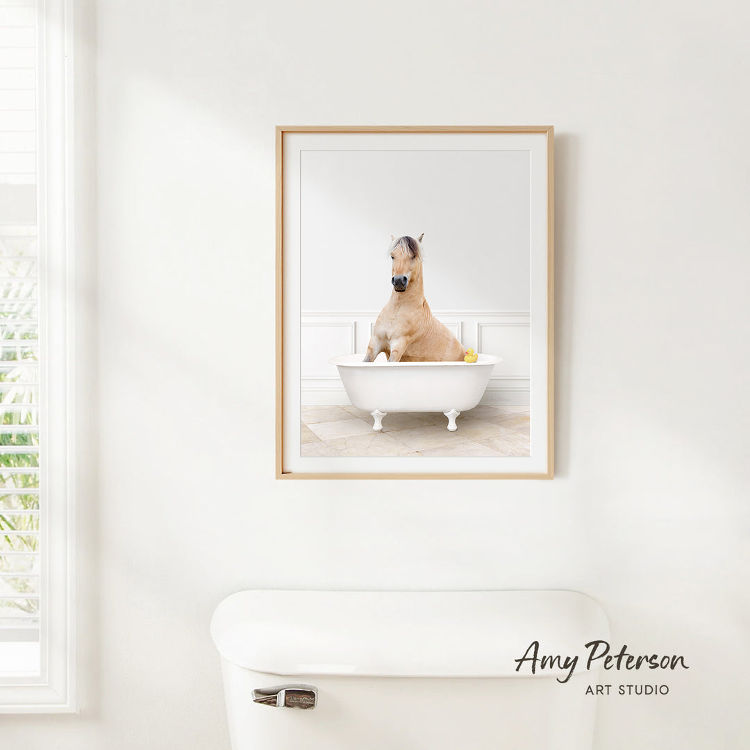 A framed photograph of a horse sitting in a bathtub, with a window and a toilet visible in the background.
