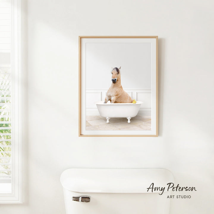 A framed photograph of a horse sitting in a bathtub, with a window and a toilet visible in the background.