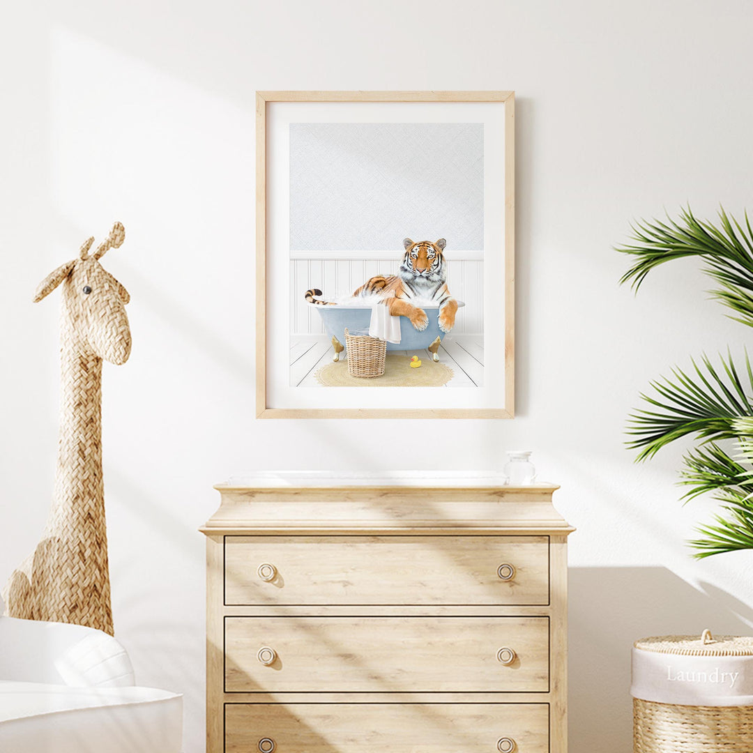 A framed image of a tiger sitting in a bathtub, surrounded by a giraffe and a plant, is displayed on a white wall above a wooden dresser.