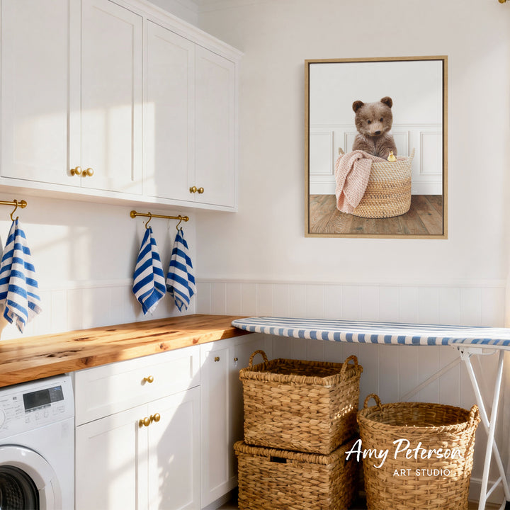 A cozy laundry room with white cabinets, a wooden countertop, and a framed image of a bear sitting in a basket.